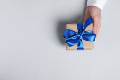 Photo of Man holding gift box with blue bow on white background, top view. Space for text