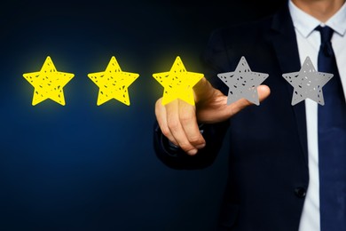 Image of Man pointing at icons of stars on dark blue background, closeup. Quality rating