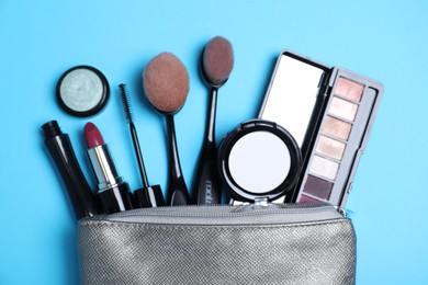 Photo of Cosmetic bag with makeup products and accessories on light blue background, flat lay