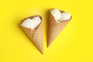 Delicious vanilla ice cream in wafer cones on yellow background, flat lay