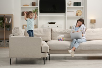 Little daughter playing while her mother working remotely on sofa at home