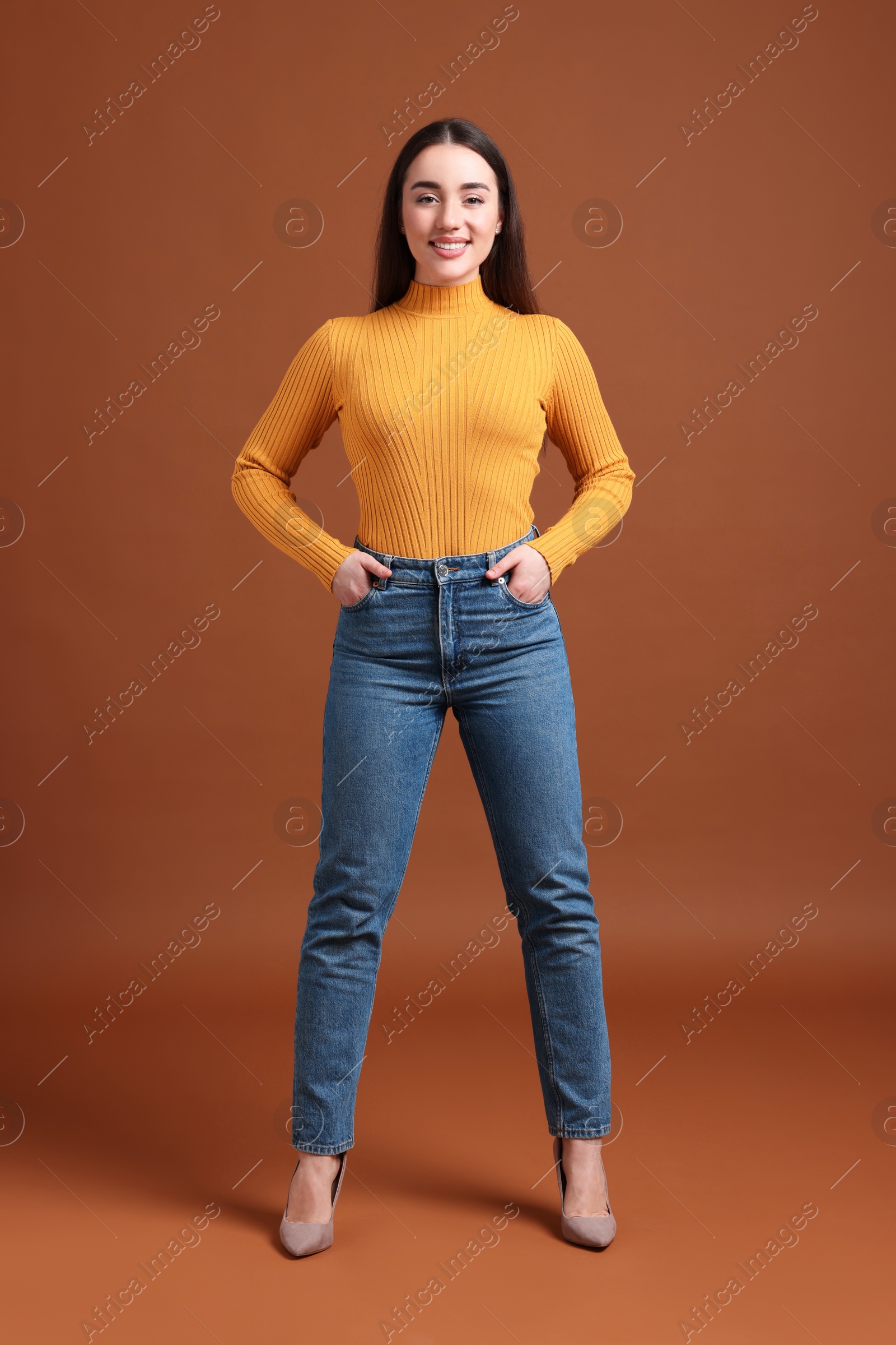 Photo of Young woman in stylish jeans on brown background