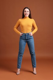Young woman in stylish jeans on brown background