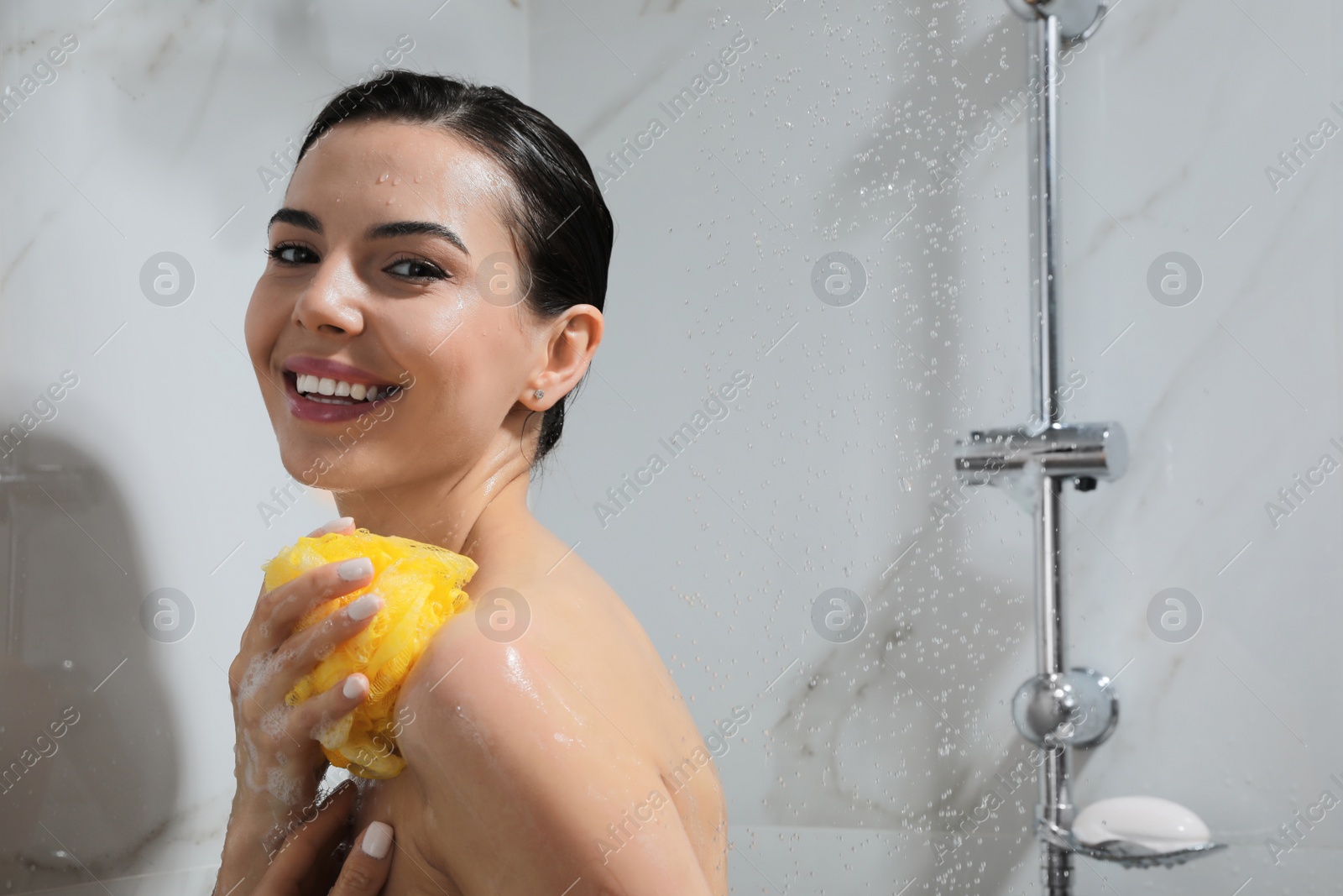 Photo of Young woman with mesh pouf taking shower at home. Space for text