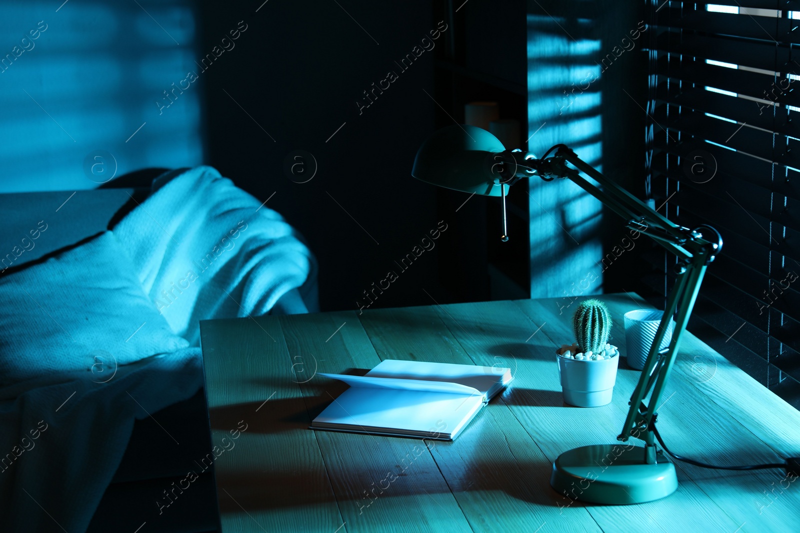 Photo of Stylish lamp and open book on wooden table at night