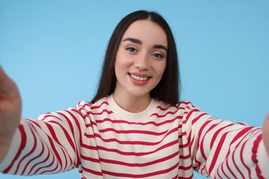 Photo of Smiling young woman taking selfie on light blue background