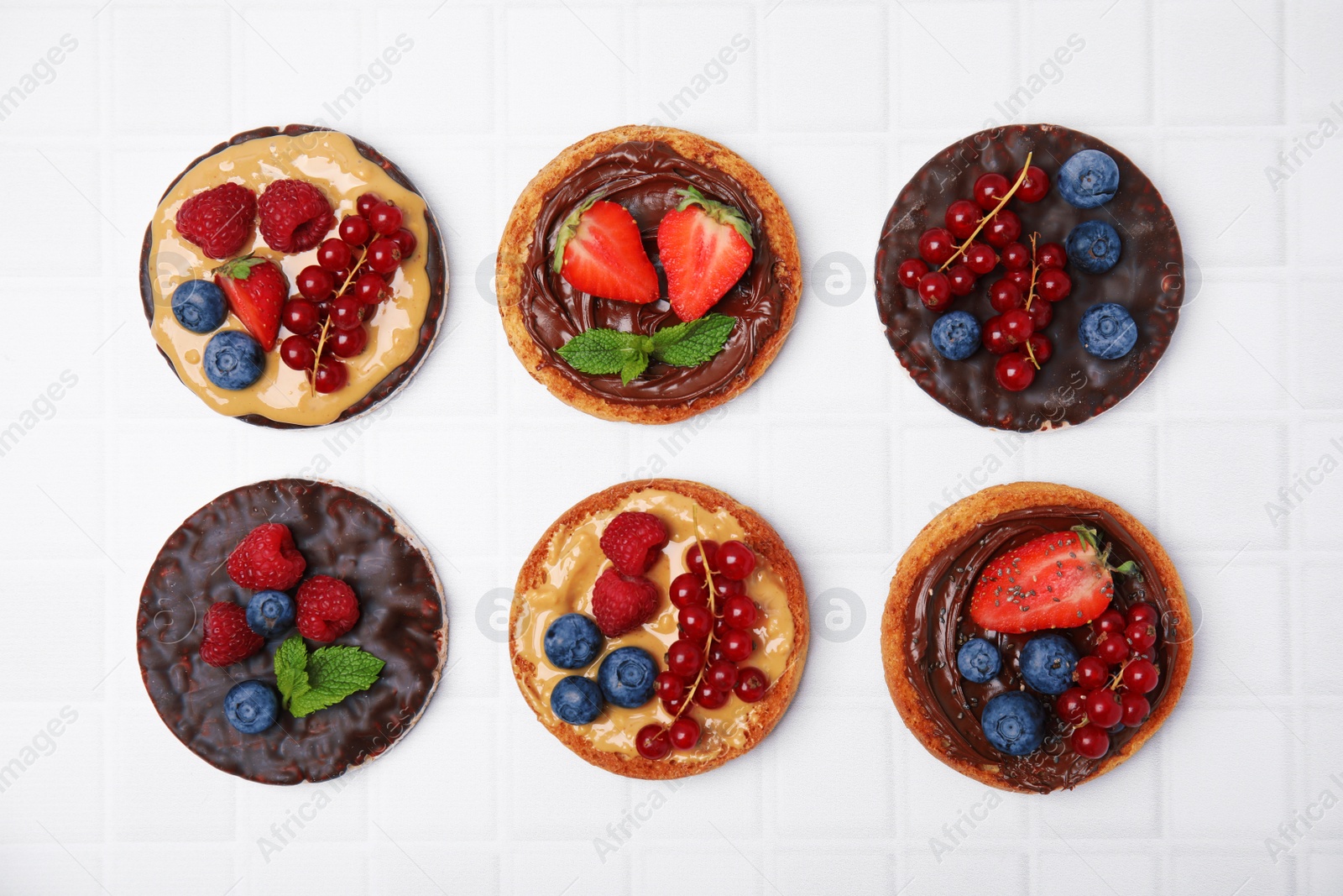 Photo of Fresh rice cakes and rusks with different toppings on white table, flat lay