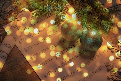 Image of Christmas and New Year music. Fir tree branch, festive balls and music sheets on wooden background, bokeh effect