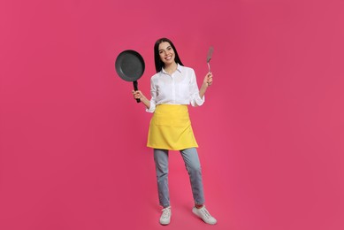 Photo of Young housewife with frying pan and spatula on pink background
