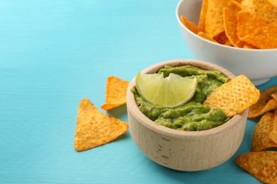 Photo of Bowl of delicious guacamole, lime and nachos chips on light blue wooden table, closeup. Space for text