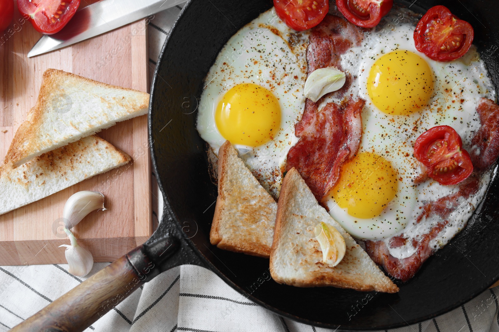 Photo of Delicious fried eggs with bacon and tomatoes in pan on table, flat lay