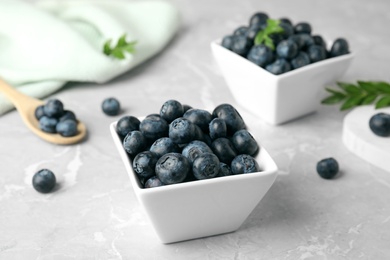 Photo of Bowls of tasty blueberries and spoon on grey marble table