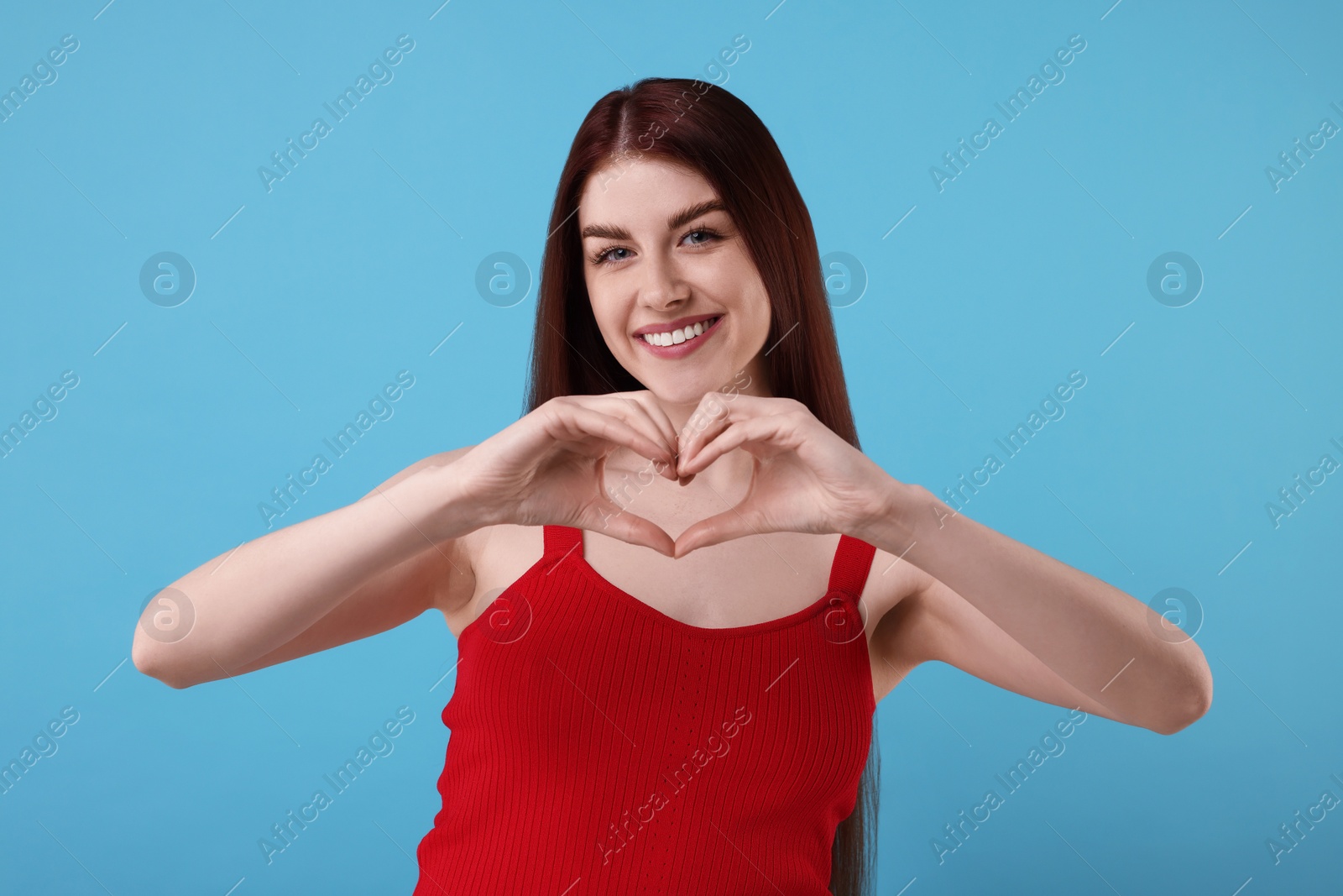 Photo of Happy young woman showing heart gesture with hands on light blue background