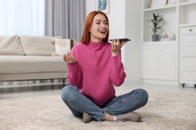 Photo of Happy woman sending voice message via smartphone on floor at home