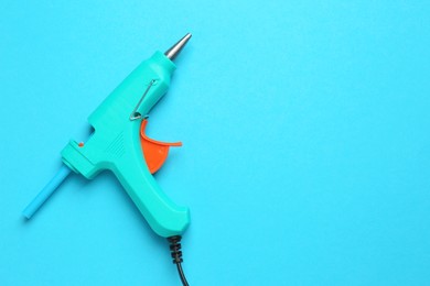 Turquoise glue gun with stick on light blue background, top view. Space for text