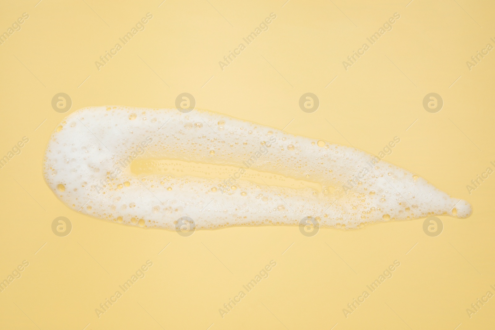Photo of Smudge of white washing foam on yellow background, top view
