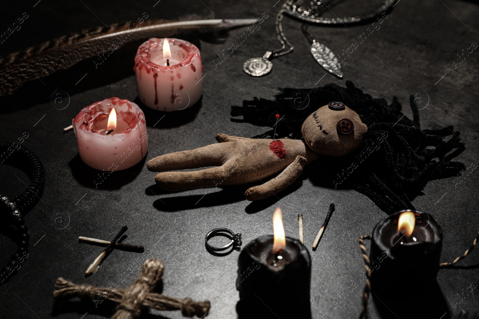 Photo of Female voodoo doll with pin in heart and ceremonial items on grey table