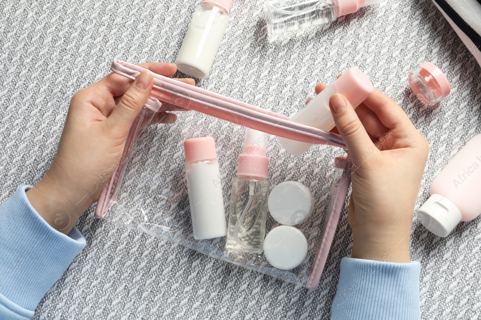 Photo of Cosmetic travel kit. Woman putting small bottle with personal care product into plastic bag on sofa, top view