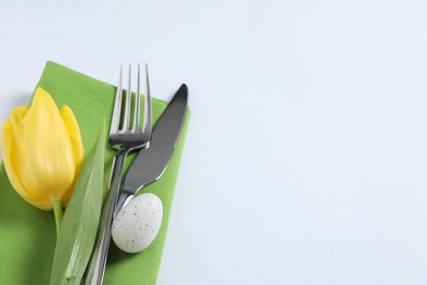 Cutlery set, Easter egg and tulip on white background, space for text. Festive table setting