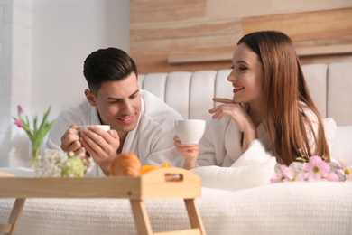 Happy couple in bathrobes having breakfast on bed at home