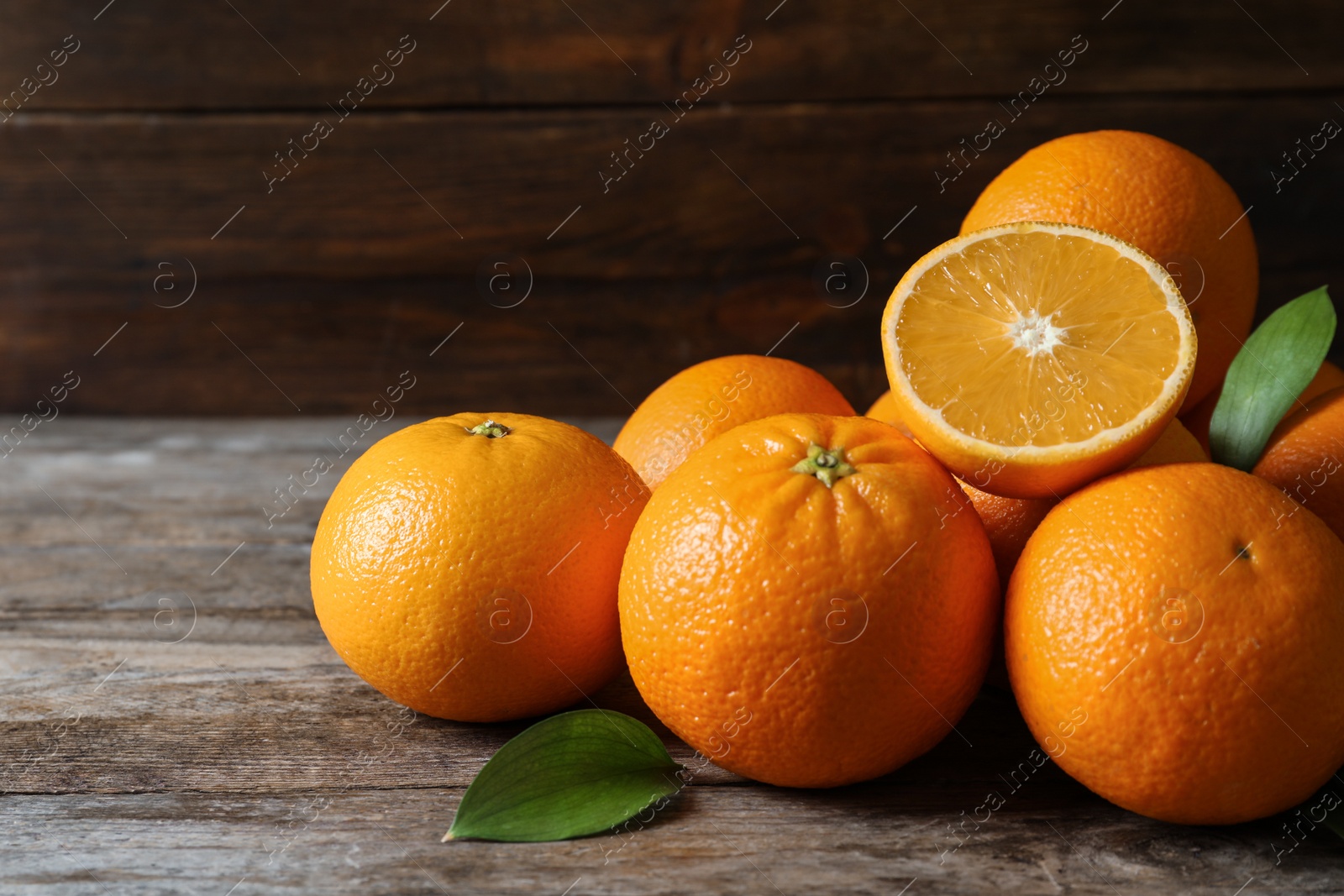 Photo of Fresh oranges with leaves on wooden table, space for text