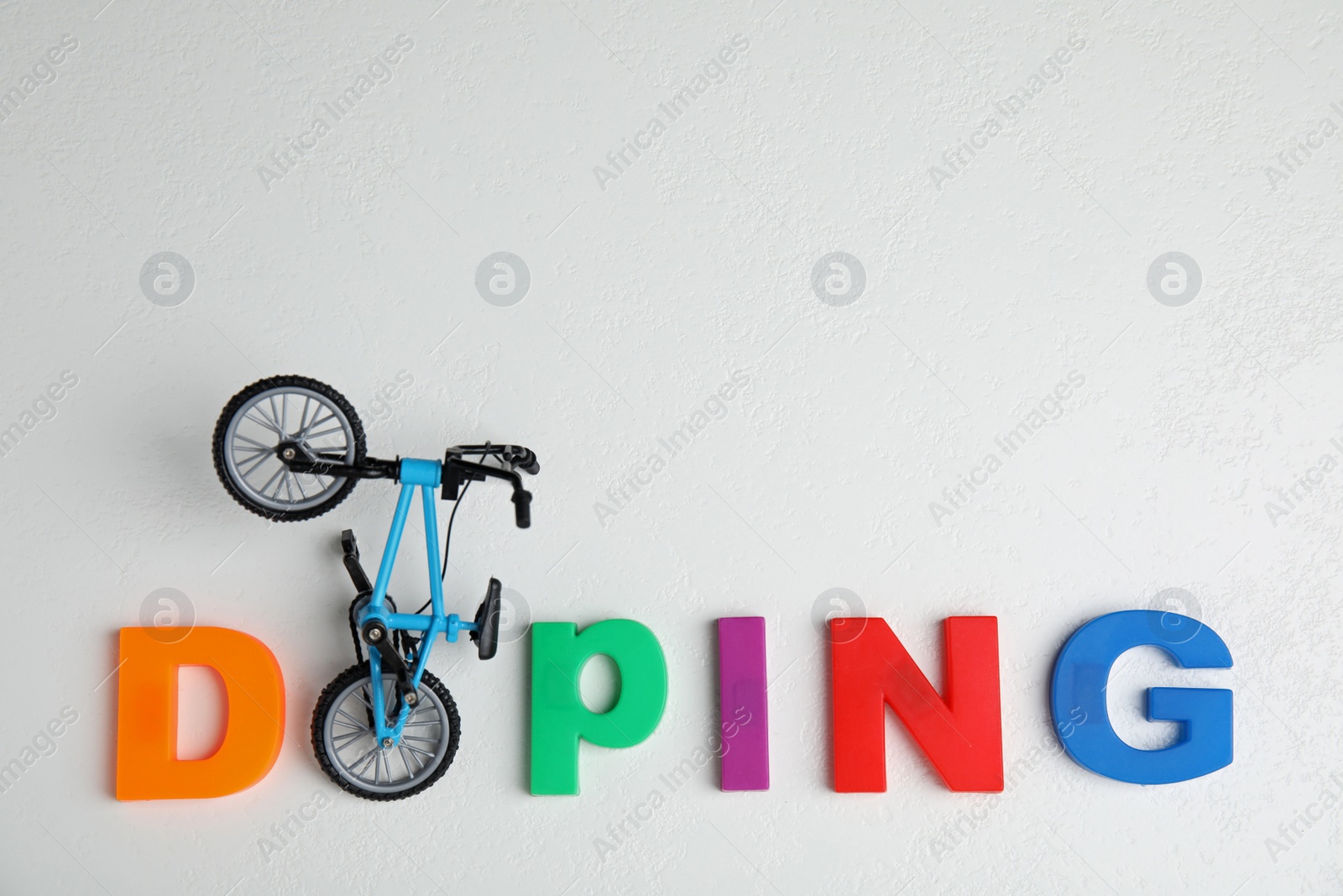 Photo of Word Doping and bicycle model on white table, flat lay. Space for text