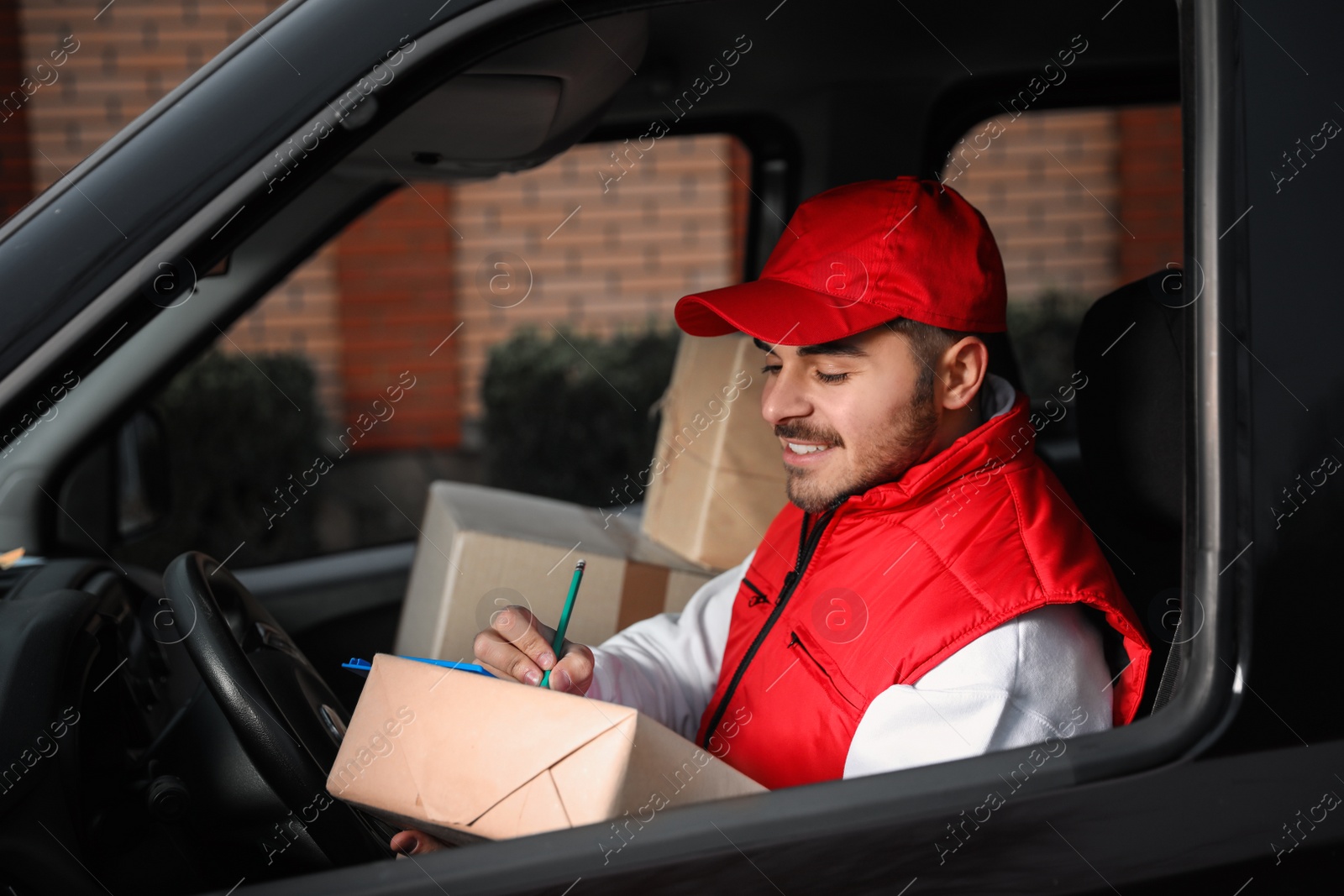 Photo of Deliveryman in uniform with parcels in car