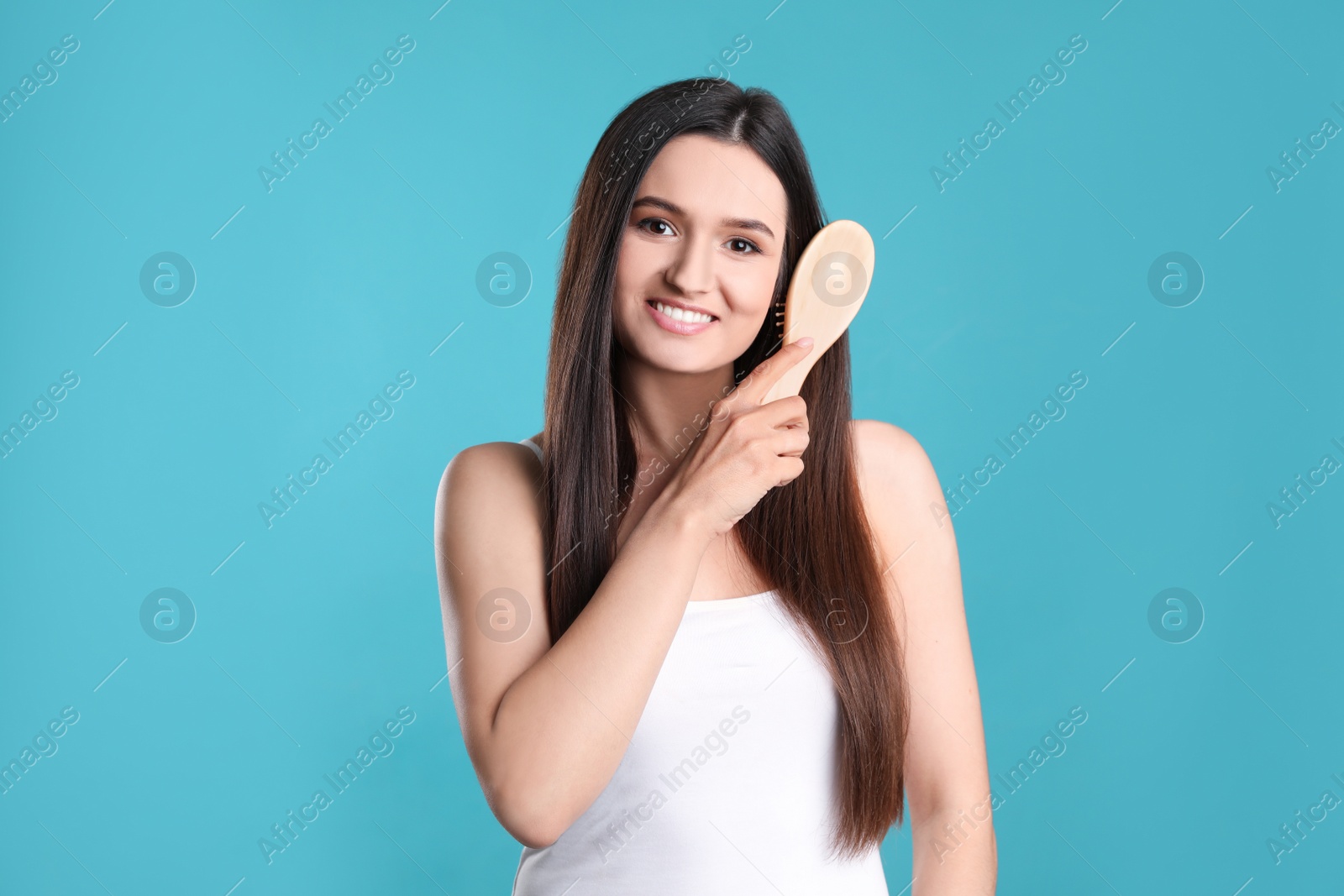 Photo of Beautiful smiling young woman with hair brush on color background