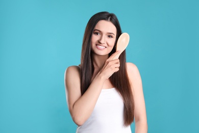 Photo of Beautiful smiling young woman with hair brush on color background