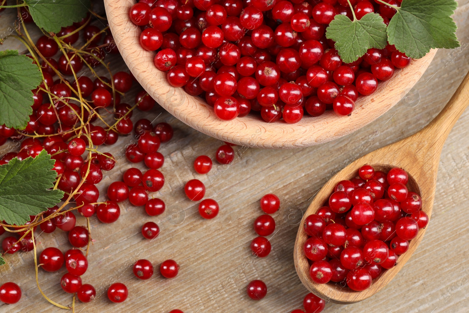 Photo of Ripe red currants and leaves on wooden table, flat lay