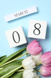 Photo of International Women's day - 8th of March. Wooden block calendar and beautiful flowers on light blue background, flat lay