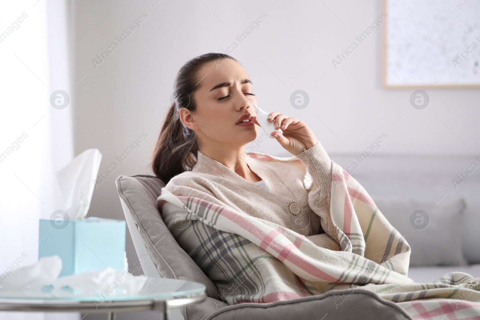 Photo of Sick young woman using nasal spray at home