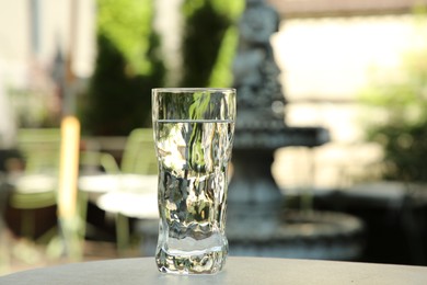Photo of Glass of fresh water on light grey table outdoors