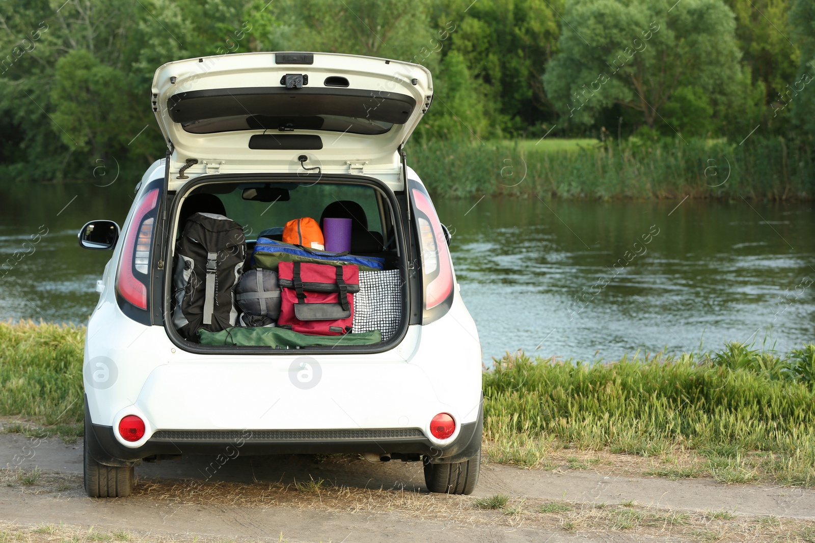 Photo of Car with camping equipment in trunk on riverbank. Space for text