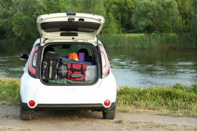 Photo of Car with camping equipment in trunk on riverbank. Space for text
