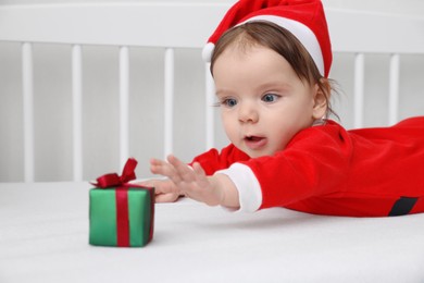 Photo of Cute baby wearing festive Christmas costume with gift box in crib