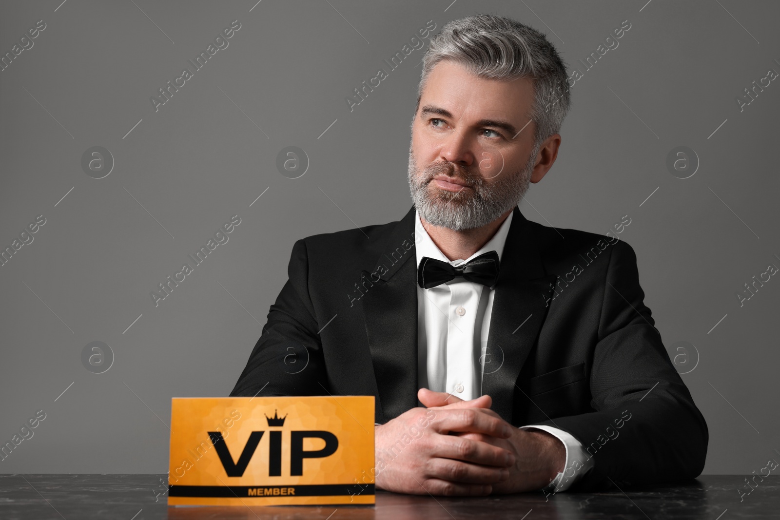 Photo of Handsome man sitting at table with VIP sign on grey background. Space for text