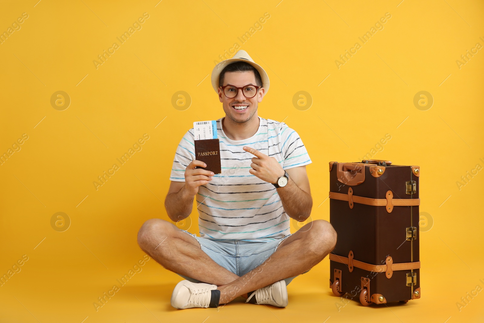 Photo of Excited male tourist holding passport with ticket near suitcase on yellow background