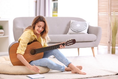 Young woman with acoustic guitar composing song in living room. Space for text