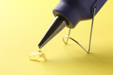Photo of Melted glue dripping out of hot gun nozzle on yellow background, closeup