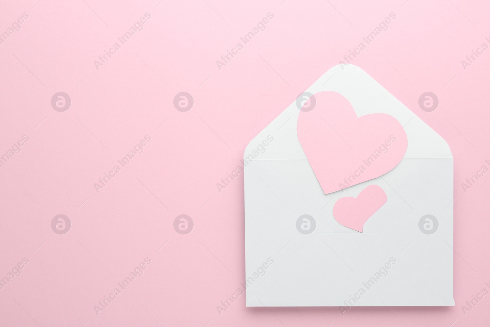 Photo of Paper hearts in envelope on pink background, top view. Space for text