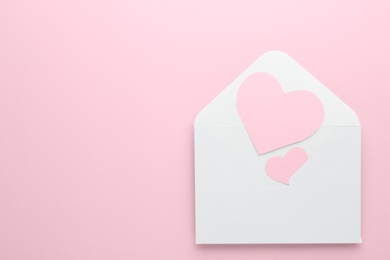 Photo of Paper hearts in envelope on pink background, top view. Space for text