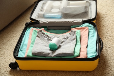 Photo of Deodorant in packed suitcase on floor indoors