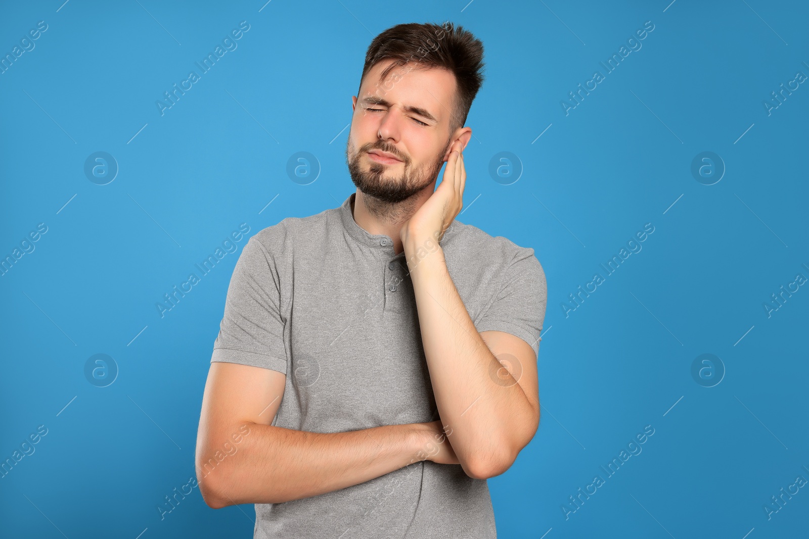 Photo of Young man suffering from ear pain on light blue background