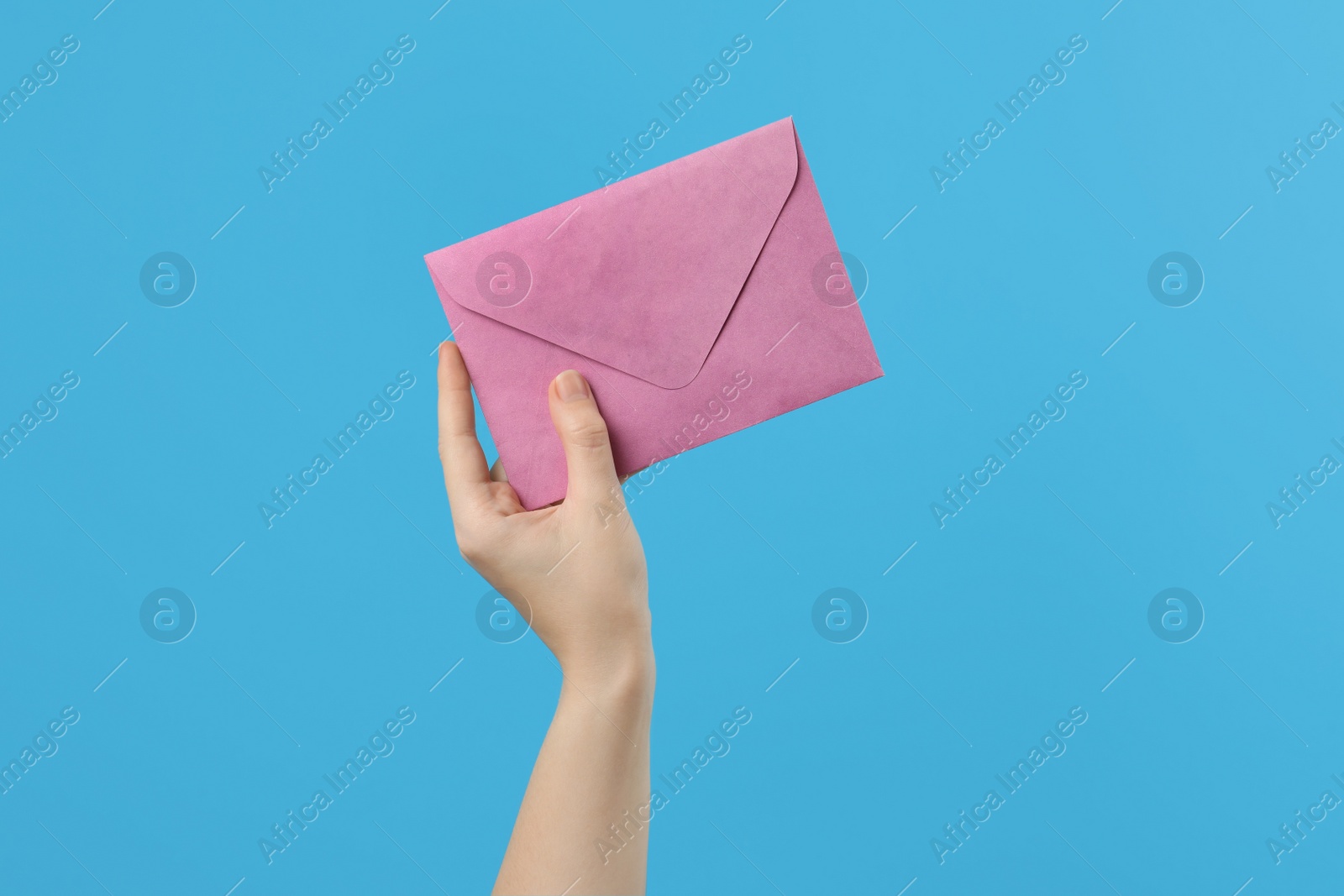 Photo of Woman holding pink paper envelope on light blue background, closeup