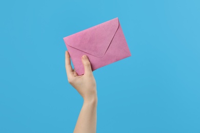 Photo of Woman holding pink paper envelope on light blue background, closeup