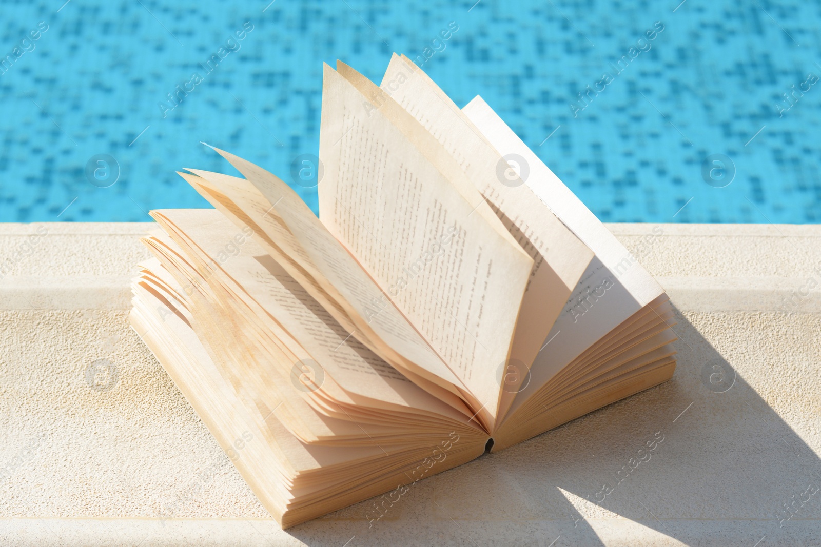 Photo of Open book on swimming pool edge during sunny day