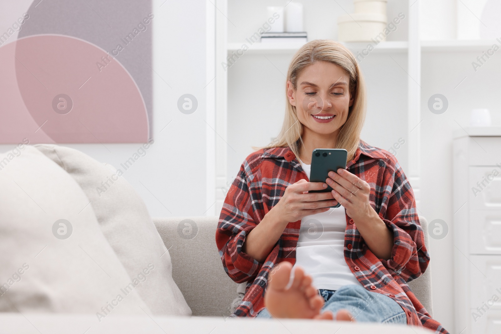 Photo of Happy woman sending message via smartphone on couch at home