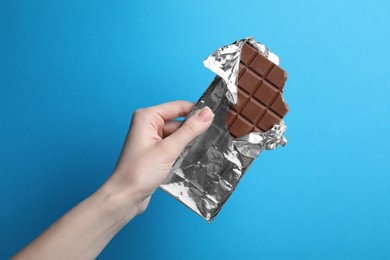 Photo of Woman holding delicious chocolate bar on light blue background, closeup