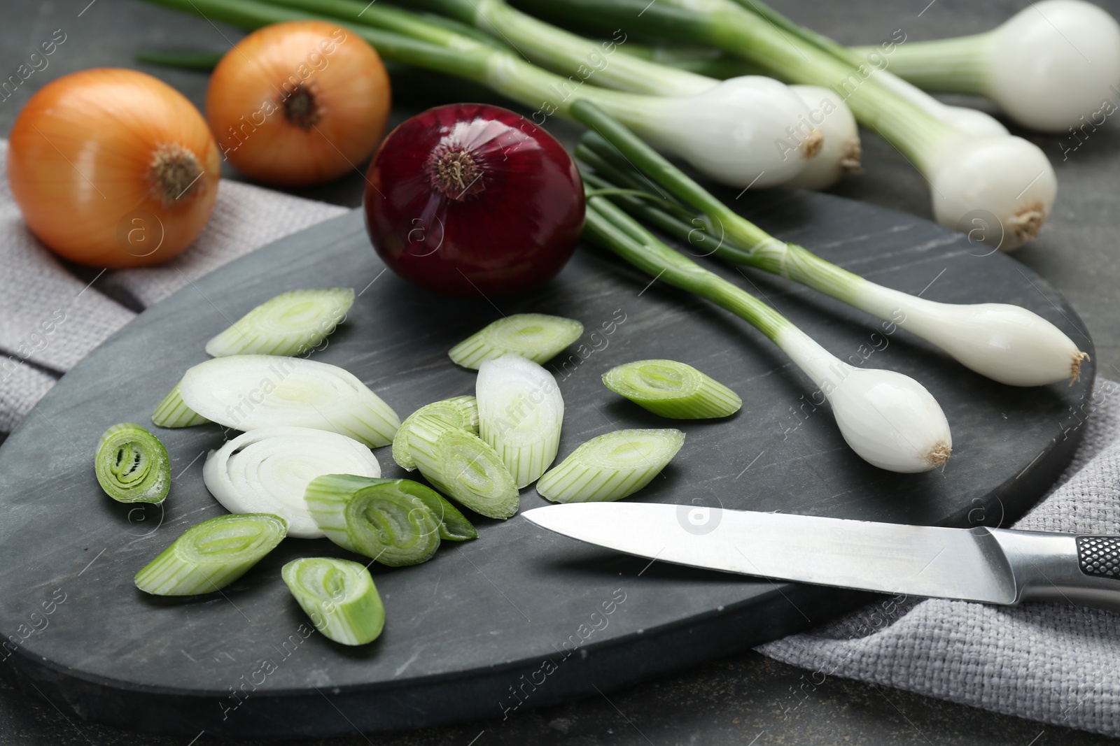 Photo of Board with different kinds and knife of onions on grey table, closeup